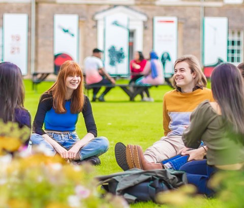 Students sitting in a circle on a patch of grass, laughing and talking.