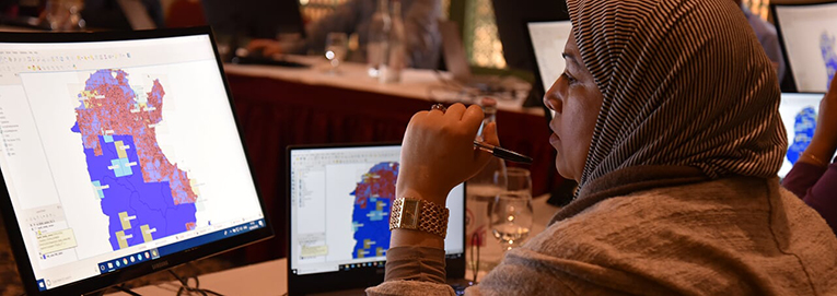 Tunisian research participant Mouna Hermassi using QGIS to map archaeological sites. A technical map is visible on her computer screens.