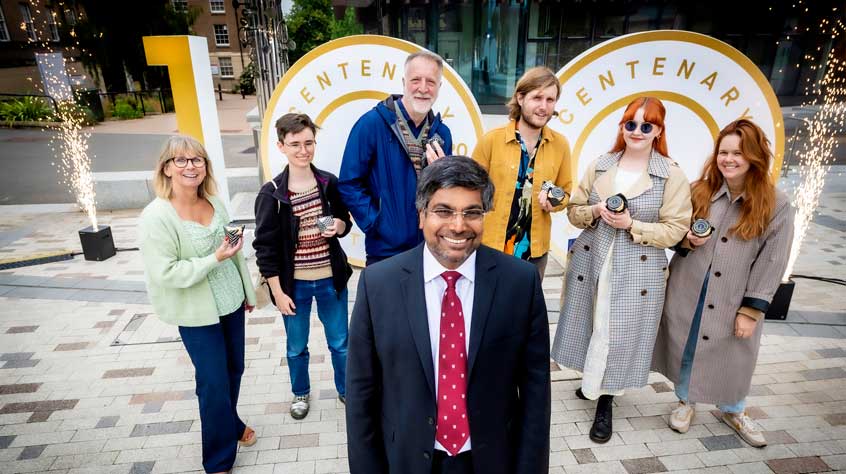 Nishan with people from the centenary launch event in front the centenary sign.