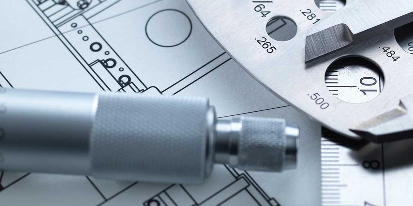 dial calipers sitting on a rule with engineering drawings
