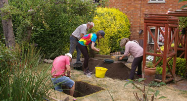 Four people working on an excavation site in a back garden of a house.