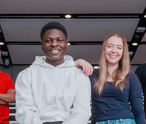 Two male and two female students in a lecture theatre smiling and looking towards the camera