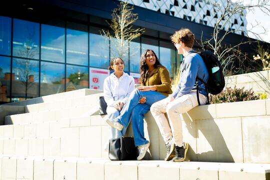 Three students sitting outside campus building in the sunshine