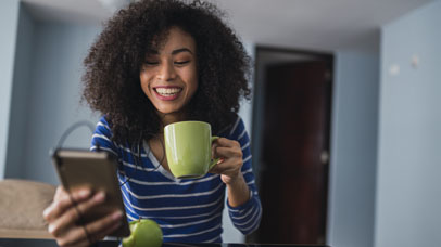 Portrait of happy young woman with coffee mug while looking at cell phone