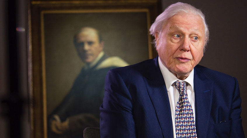 Sir David Attenborough being interviewed, a portrait of his father Frederick hangs behind him.