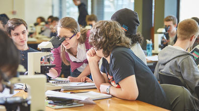 students and teacher looking through microscope in busy classroom