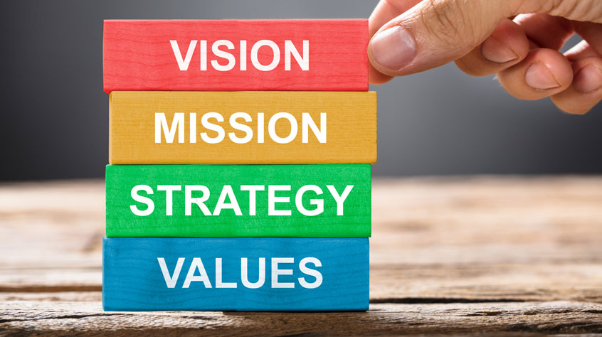 Closeup of hand building colorful blocks of vision mission strategy and values on wood