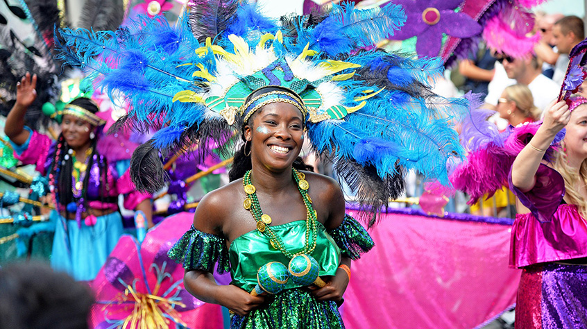 A performer at Leicester's Caribbean Carnival, wearing blue feathers and surrounded by pink and purple banners