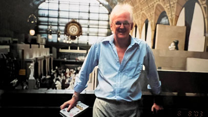 A man holding a book in a large room with lots of paraphernalia around him