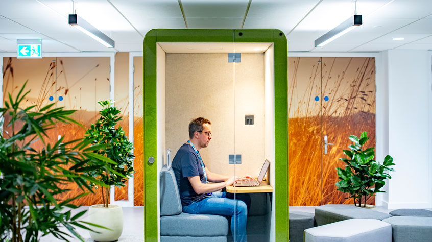 Person sitting working on a laptop in a private booth in an office.