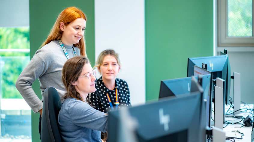 Three people gathered around a computer in an office.