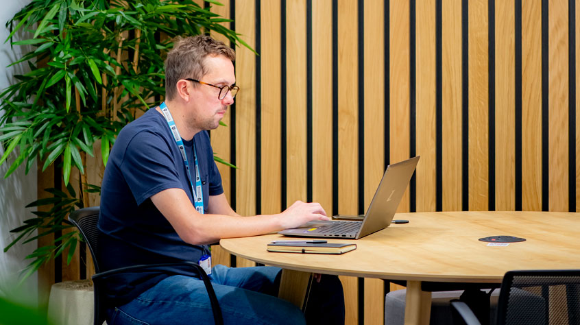Person working on a laptop on a table in an open plan office.