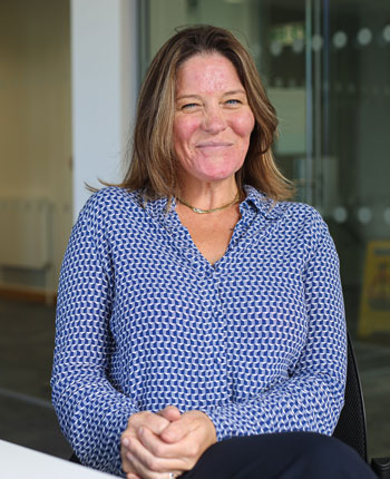 A woman wearing a blue shirt, sitting in a chair and smiling.