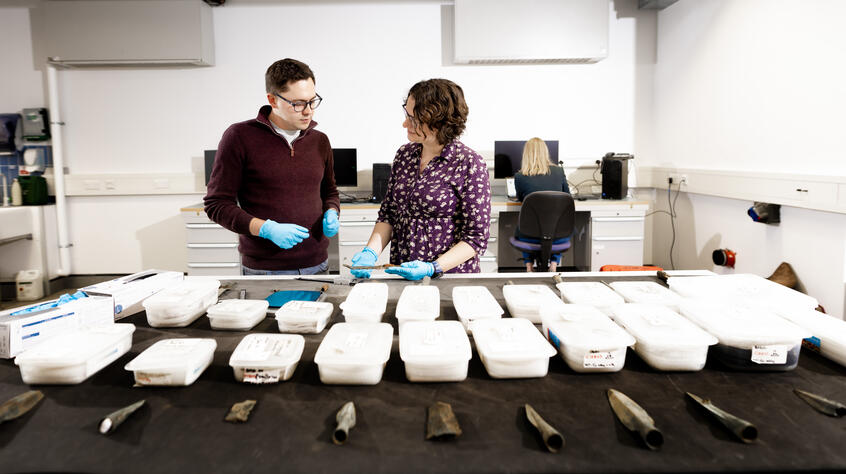 Two people behind a table of archaeological artefacts