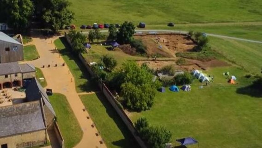 Birds-eye view of excavations with tents next to the dirt and large building