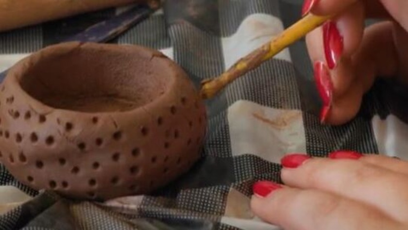 Red painted finger-nailed hands making round marks on a clay pot