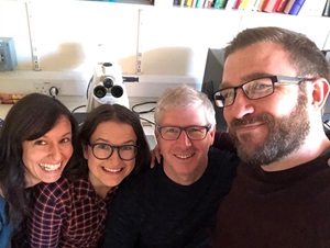A photo of the project team in a lab, posing in front of a microscope. Left to right is Christina Tsoraki, Rachel Crellin, Huw Barton and Ollie Harris.