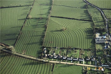 An aerial photograph of a modern-day village set within a preserved open field system with surviving ridge-and-furrow