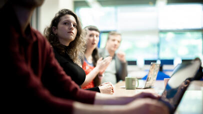 Desk of students with one individual focussed looking towards the camera