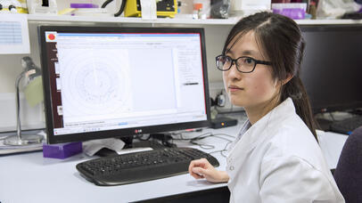 Student in lab coat at desk looking to the side
