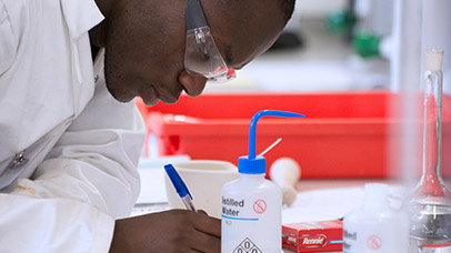 student writing and is surrounded by chemical equipment