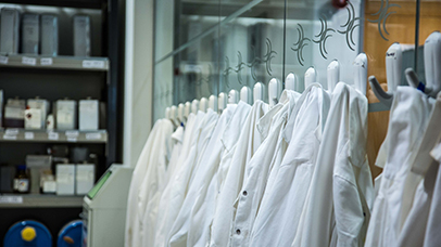 Lab coats on pegs against a glass lab wall with the logo of Infineum etched into the glass