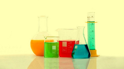 A range of scientific glassware containing colourful liquids, on top of a reflective surface against a yellow background