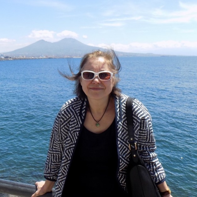 Elena Piletska, pictured wearing sunglasses in front of deep blue water on a sunny day, with mountains in the background.