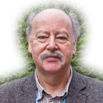 Photograph of Rob Hillman, wearing a suit jacket and standing in front of a bush