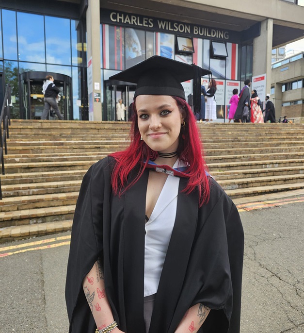 Diana Gaman wearing graduation gown and hat, standing in front of the Charles Wilson Building.
