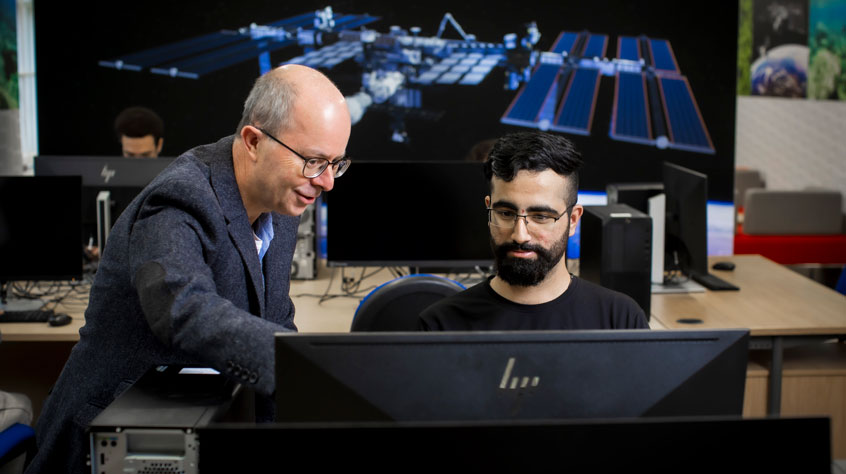An academic pointing to the screen whilst a student observes