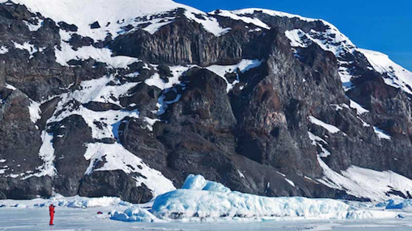 Geologist standing in front of volcanic rocks at Cape Washington, Antarctica, erupted 2.7 million years ago when the ice sheet was much thicker. Photo by John Smellie.