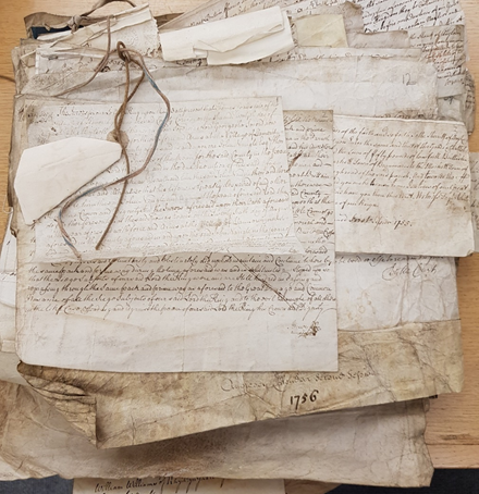 Bundle of mid 18th century manuscript pages, layered on top of one another, with an untied string at the side.