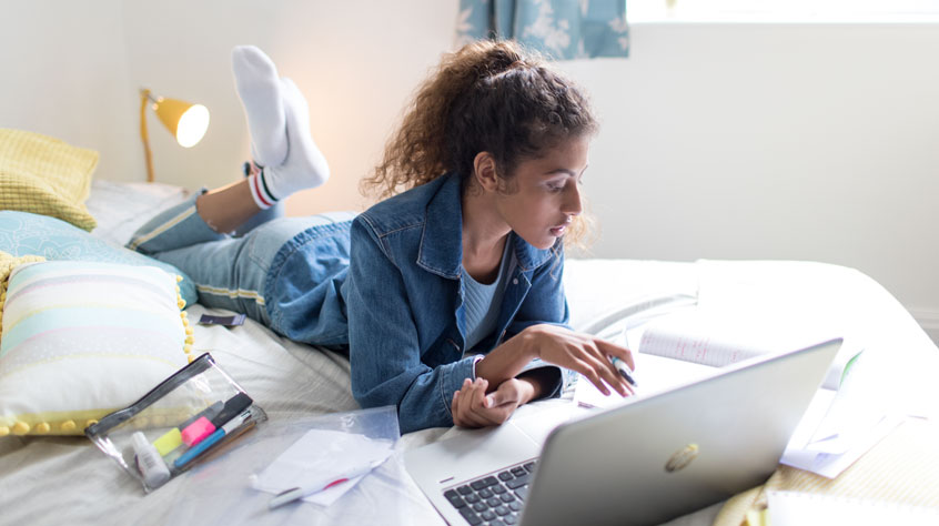 Student laying on a bed on a laptop