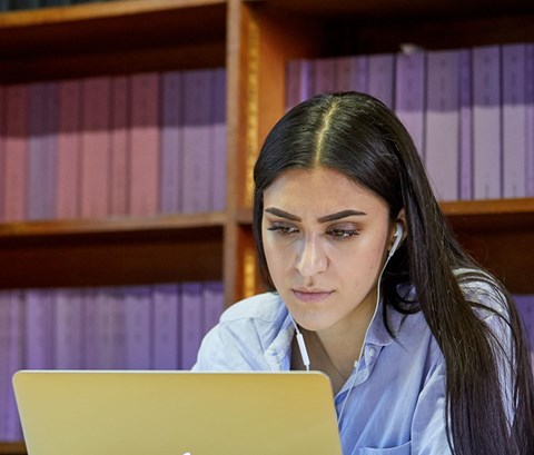 Student working on a laptop with a backdrop of the law library behind him.