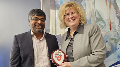 Two people, each representing the University of Leicester and Humber Polytechnic, smile while one holds a plaque with a crest on it.