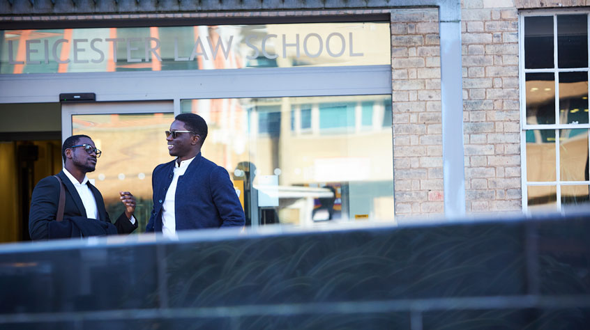 Two students standing outside the Leicester Law School building and talking