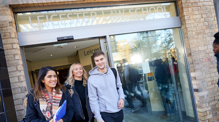Three students walking out of a building called 'Leicester Law School'