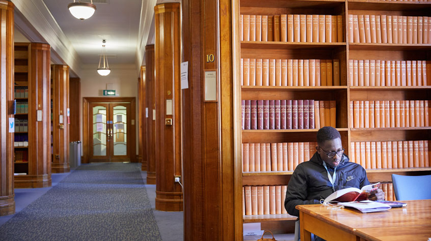 A student sitting at a table in an ornate, wooden library