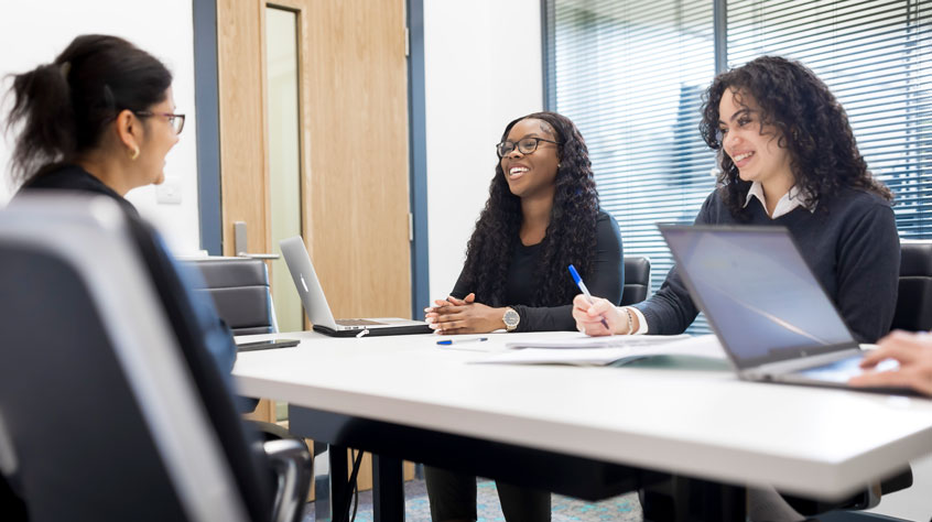 Three students sitting at a conference table and smiling