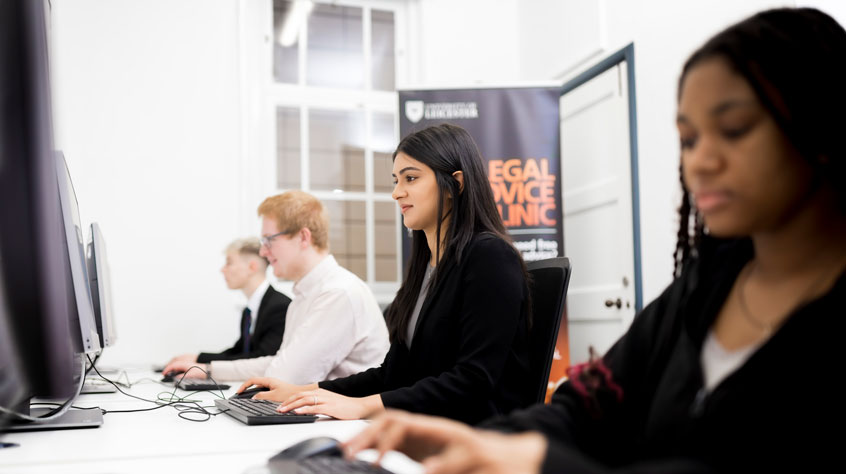 Four students sitting in a row, all working on computers.