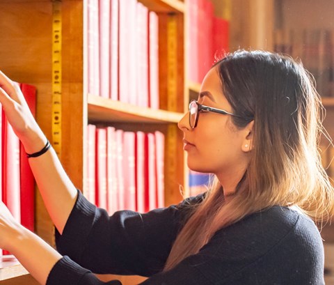Student taking a large book off a shelf in an ornate library
