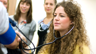 Student wearing a stethoscope, listening to a patient's chest 