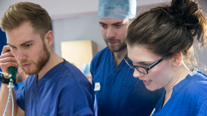 Three students in scrubs working on a patient