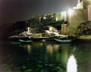 A shipping dock at night with a spotlight reflecting off the water and boats moored and empty