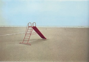 Photograph of a child's red slide on an empty beach and the sea in the background