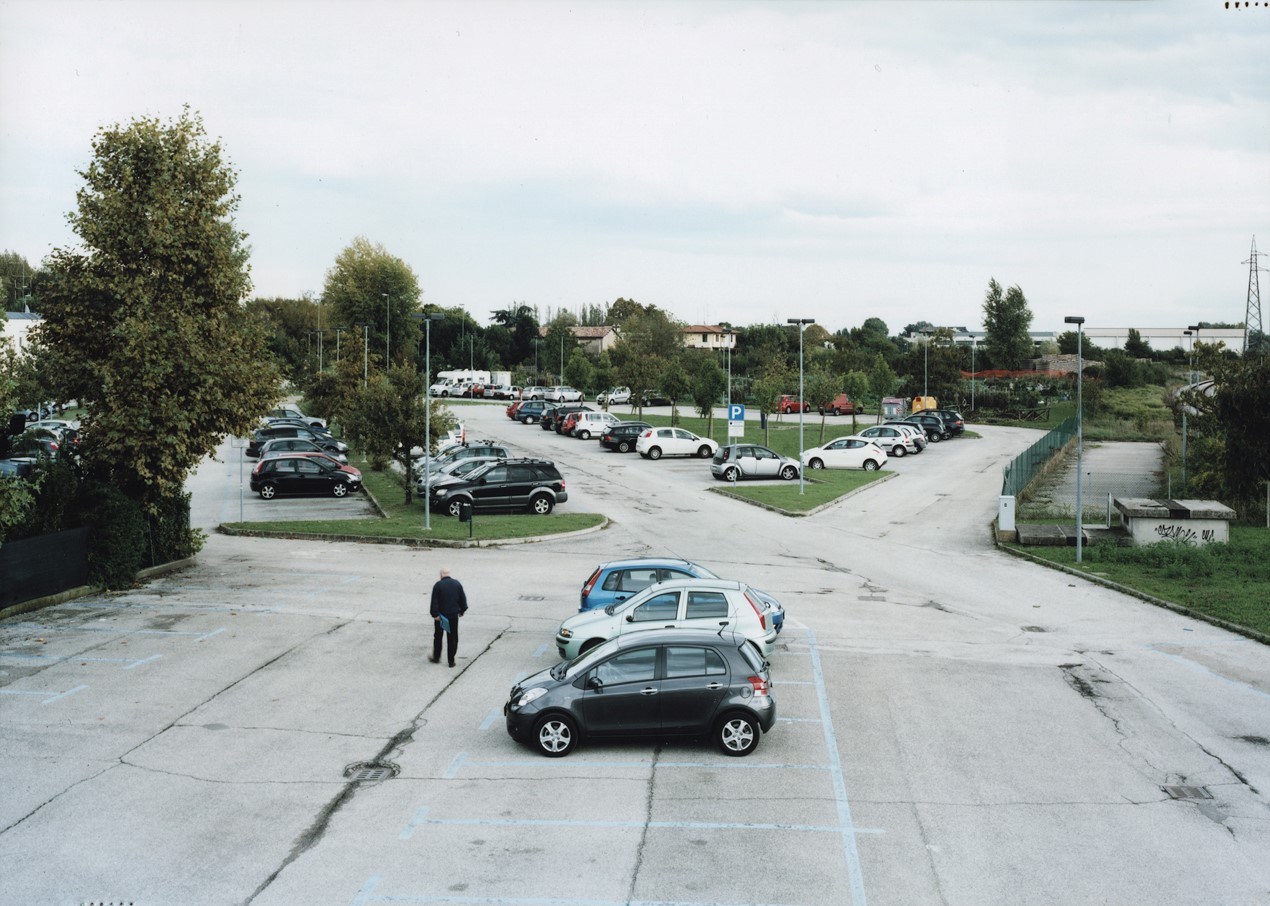 Photograph of a car park, a person walking way from their vehicle, and two roads leading away deeper into the lot