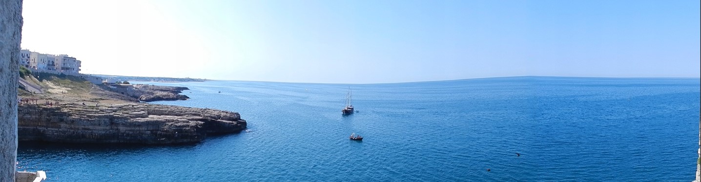 A wide panoramic photograph of the ocean and a rocky coastline with boats sailing nearby