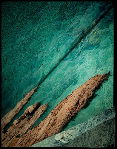 Photographic artwork based on coastal seascape featuring jagged rocks, deep and dark colour contrast between ocean, beach, rocks and stone wall