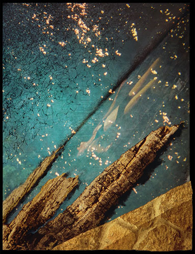 Photographic artwork based on coastal seascape featuring jagged rocks, deep and dark colour contrast between ocean, beach, rocks and stone wall